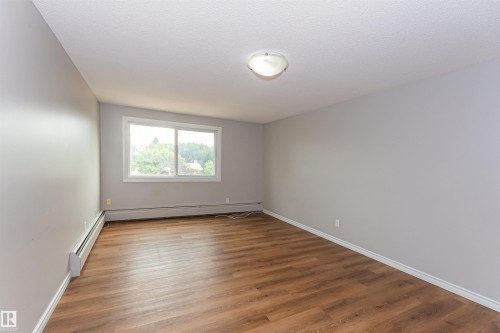 Spacious room featuring wood-finish flooring, light grey walls, and a large window with white trim - Edmonton, AB - Indoor Photo Showing Other Room