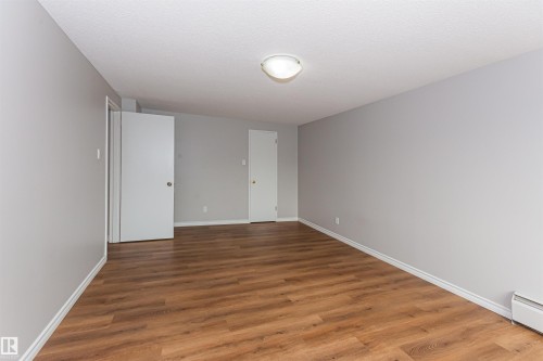 Spacious room featuring wood-finish flooring, light grey walls, white baseboards, and two white doors - Edmonton, AB - Indoor Photo Showing Other Room