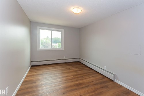 Room featuring wood-finish flooring, light gray walls, white trim, and a white-framed window - Edmonton, AB - Indoor Photo Showing Other Room
