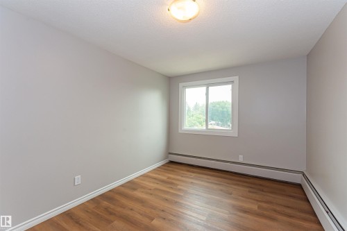 Interior space featuring light gray walls, wood-finish flooring, white baseboards, and a white-framed window - Edmonton, AB - Indoor Photo Showing Other Room