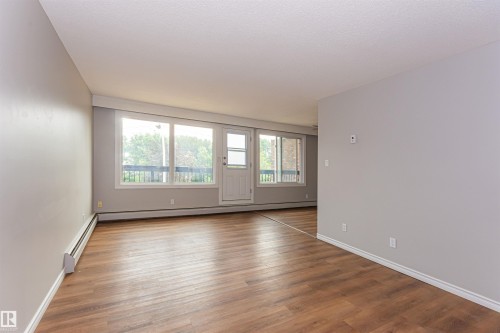 Spacious room featuring wood-finish flooring, light grey walls, and white baseboards - Edmonton, AB - Indoor Photo Showing Other Room