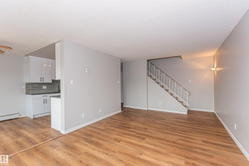 Open-concept living area featuring wood-finish flooring, a contemporary staircase with white railing, and a wall-mounted sconce - Edmonton, AB - Indoor