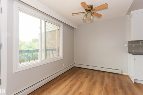 Bright living area featuring a large window with white trim, wood-finish flooring, a ceiling fan with integrated lighting, and neutral wall paint - Edmonton, AB - Indoor Photo Showing Other Room