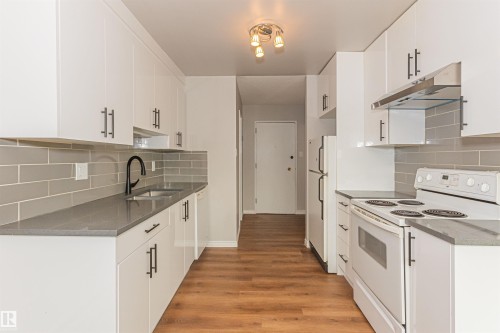 Kitchen featuring white cabinetry, gray countertops, a gray subway tile backsplash, wood-finish flooring, and a stainless steel range hood - Edmonton, AB - Indoor Photo Showing Kitchen