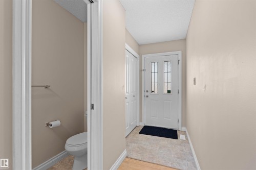 Entryway featuring a white paneled door with glass inserts, adjacent to a powder room with a toilet and wall-mounted towel bar, all set on light-toned flooring - 15504 102 Avenue Nw, Edmonton, AB 