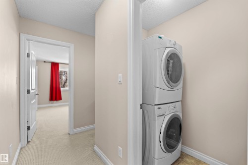 Integrated stacked washer and dryer unit, neutral wall paint, and light-colored carpeted flooring - 15504 102 Avenue Nw, Edmonton, AB 