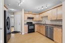 Kitchen featuring wood-finish flooring, light wood cabinetry, black appliances, a stainless steel dishwasher, and track lighting - 15504 102 Avenue Nw, Edmonton, AB 
