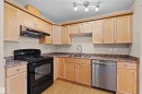 Kitchen featuring wood-finish flooring, light wood cabinetry, a double basin stainless steel sink, a stainless steel dishwasher, and a black electric range with an overhead vent - 15504 102 Avenue Nw, Edmonton, AB 
