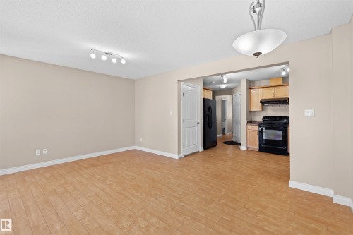 Wood-finish flooring throughout, track lighting, ceiling-mounted light fixture, light wood cabinetry, and black appliances - 15504 102 Avenue Nw, Edmonton, AB 