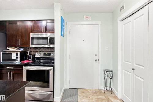 Kitchen featuring wood-finish cabinetry, stainless steel appliances, and a tiled backsplash - #413 18126 77 St Nw, Edmonton, AB 