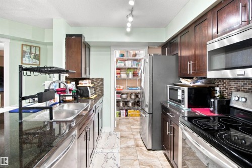 Dark wood-finish cabinetry, stainless steel appliances, dark granite countertops, tile backsplash, and built-in pantry - #413 18126 77 St Nw, Edmonton, AB 