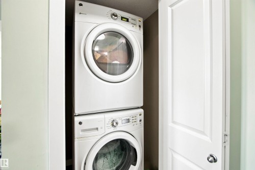 Stacked washer and dryer unit, white paneled door, and light wall finishes - #413 18126 77 St Nw, Edmonton, AB 