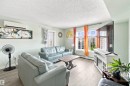 Light wood-finish flooring, wall-mounted air conditioning unit, white trim windows, and a built-in media console - #413 18126 77 St Nw, Edmonton, AB 