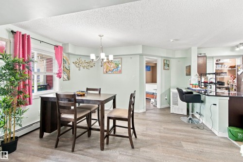 Wood-finish flooring, recessed lighting, and a modern chandelier illuminate the dining area and kitchen bar - #413 18126 77 St Nw, Edmonton, AB 
