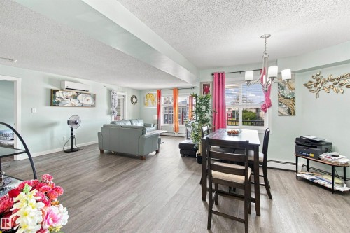 Open-concept living and dining area featuring wood-finish flooring, a wall-mounted climate control unit, and a suspended chandelier - #413 18126 77 St Nw, Edmonton, AB 