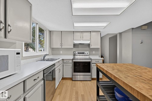 Kitchen featuring light wood-finish flooring, white countertops, gray cabinetry, stainless steel appliances, and a butcher block island - 17919 78 Avenue Nw, Edmonton, AB 