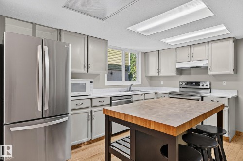Kitchen featuring stainless steel appliances, light gray cabinetry, white countertops, a butcher block island, and wood-finish flooring - 17919 78 Avenue Nw, Edmonton, AB 