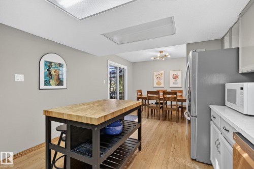 Kitchen island with wood-finish countertop, wood-finish flooring, recessed lighting, white cabinetry, and sliding glass door - 17919 78 Avenue Nw, Edmonton, AB 