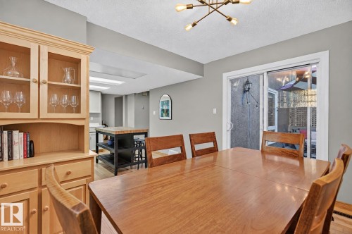 Dining area with wood-finish flooring, built-in display cabinetry, a modern ceiling light fixture, and a sliding glass door - 17919 78 Avenue Nw, Edmonton, AB 