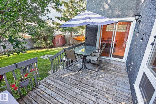 Expansive wooden deck with railing, featuring a glass sliding door, stucco exterior, and a grassy yard beyond - 17919 78 Avenue Nw, Edmonton, AB 