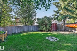 Expansive green lawn with a wood privacy fence, mature trees, garden bed, and a storage shed - 