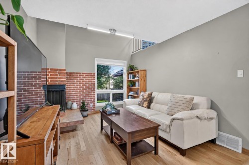 Brick-clad fireplace with hearth, wood-finish flooring, vaulted ceiling, and ample natural light from the window - 17919 78 Avenue Nw, Edmonton, AB 