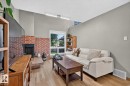Brick-clad fireplace with hearth, wood-finish flooring, vaulted ceiling, and ample natural light from the window - 17919 78 Avenue Nw, Edmonton, AB 