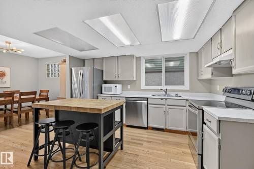 Kitchen featuring wood-finish flooring, recessed lighting, a kitchen island with a butcher block countertop, stainless steel appliances, and light-toned cabinetry - 17919 78 Avenue Nw, Edmonton, AB 