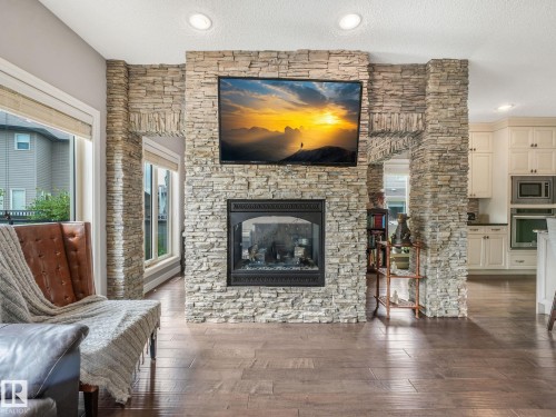 A dramatic real-stone fireplace serves as the stunning centerpiece - the grand archway creates seamless flow between the two spaces while providing natural separation when desired — allowing both sides to enjoy the warmth and ambiance of the fireplace. - 3711 Westcliff Way Sw, Edmonton, AB 