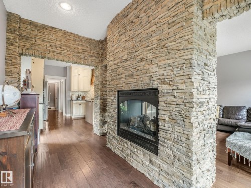 A dramatic real-stone fireplace serves as the stunning centerpiece - the grand archway creates seamless flow between the two spaces while providing natural separation when desired — allowing both sides to enjoy the warmth and ambiance of the fireplace. - 3711 Westcliff Way Sw, Edmonton, AB 