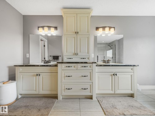 A luxurious primary ensuite bathroom featuring his-and-hers vanities, elegant cabinetry, and a spacious layout. Enjoy a deep soaking tub beside a large window, plus a generous glass-enclosed double shower — the perfect blend of comfort and elegance. - 3711 Westcliff Way Sw, Edmonton, AB 