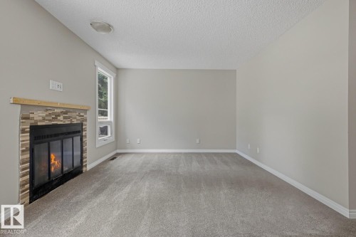 Built-in fireplace with a tile surround and wood mantel, neutral wall paint, textured ceiling, and a large window - 10621 Beaumaris Road Nw, Edmonton, AB 