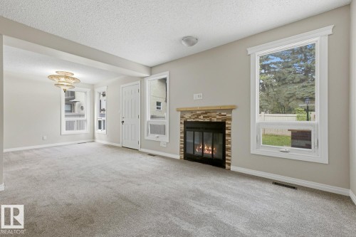 Recessed fireplace with stone surround, wood mantel, neutral carpeting, white trim windows, and a decorative ceiling light fixture - 10621 Beaumaris Road Nw, Edmonton, AB 