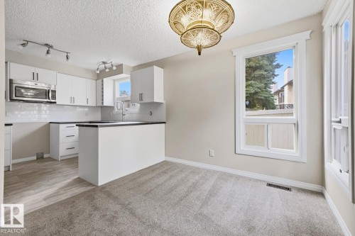 Modern kitchen featuring white cabinetry, stainless steel microwave, black countertops, white subway tile backsplash, and wood-finish flooring - 10621 Beaumaris Road Nw, Edmonton, AB 