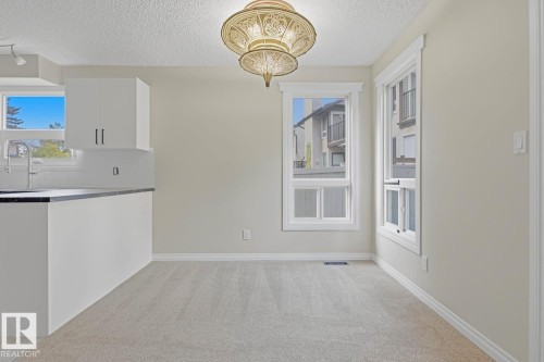 Carpeted room with a decorative chandelier, dual windows with white trim, and a built-in kitchen island featuring a dark countertop and white cabinetry - 10621 Beaumaris Road Nw, Edmonton, AB 