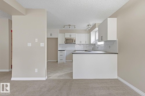 Kitchen featuring white cabinetry, dark countertops, subway tile backsplash, and stainless steel microwave - 10621 Beaumaris Road Nw, Edmonton, AB 