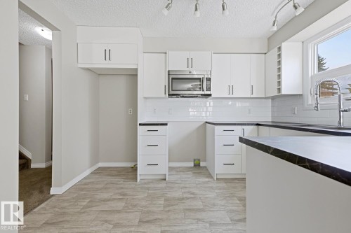 Kitchen featuring white cabinetry, dark countertops, a tile backsplash, stainless steel microwave, and track lighting - 10621 Beaumaris Road Nw, Edmonton, AB 
