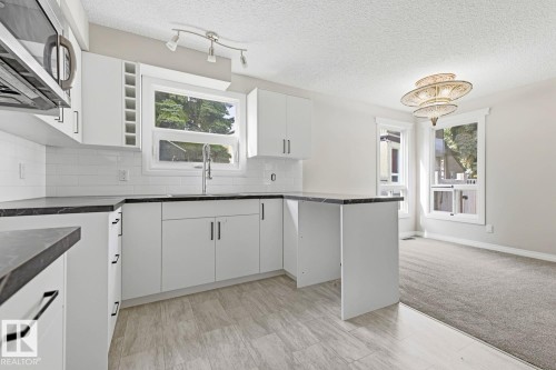 Contemporary kitchen featuring white cabinetry, dark countertops, a white subway tile backsplash, and stainless steel appliances - 10621 Beaumaris Road Nw, Edmonton, AB 