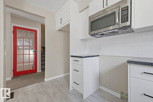White shaker cabinetry with dark hardware, stainless steel microwave, subway tile backsplash, and light wood-finish flooring - 10621 Beaumaris Road Nw, Edmonton, AB 