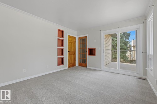 Neutral wall paint, light gray carpeting, wood panel door, built-in shelving, and sliding glass door to a balcony - 10621 Beaumaris Road Nw, Edmonton, AB 
