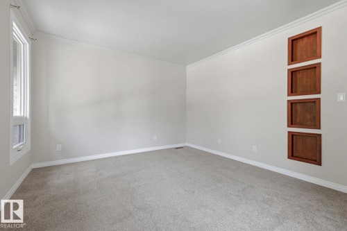 Neutral wall paint, light gray carpeting, a tall window with white trim, and built-in wood-finish wall recesses - 10621 Beaumaris Road Nw, Edmonton, AB 