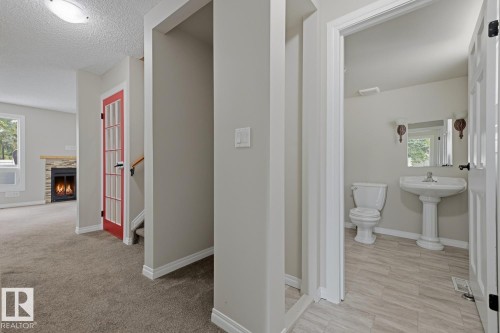 Pedestal sink with wall-mounted sconce lighting, wood-finish flooring, and a red interior door - 10621 Beaumaris Road Nw, Edmonton, AB 