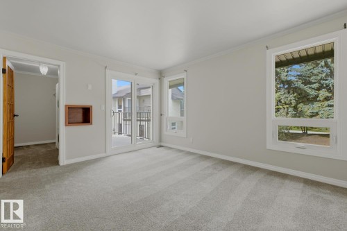 Sliding glass door access to an exterior deck, multiple windows with white trim, light gray carpet, wood-finish door, and built-in wall niche - 10621 Beaumaris Road Nw, Edmonton, AB 