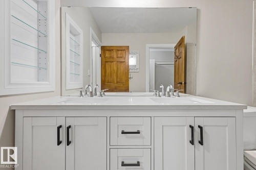 Dual integrated sinks with chrome fixtures, white shaker cabinetry, matte black hardware, and a large wall-mounted mirror - 10621 Beaumaris Road Nw, Edmonton, AB 