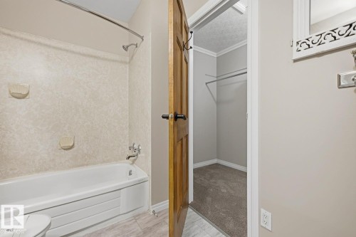 Full bathtub with an integrated shower, chrome fixtures, and a textured shower surround - 10621 Beaumaris Road Nw, Edmonton, AB 