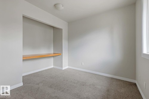 Built-in wood-finish shelving, flush-mount ceiling light, window with trim, light-toned carpeting, and neutral wall paint - 10621 Beaumaris Road Nw, Edmonton, AB 