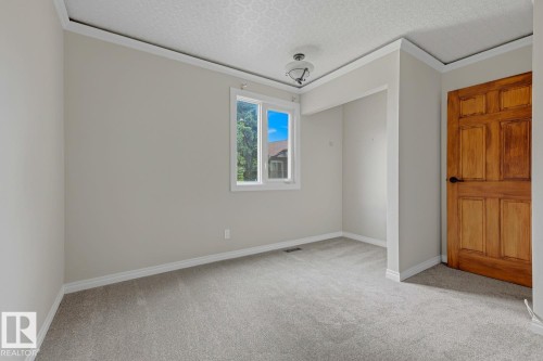 Neutral wall paint, light gray carpeting, natural wood-paneled door, bright window, and decorative ceiling fixture - 10621 Beaumaris Road Nw, Edmonton, AB 