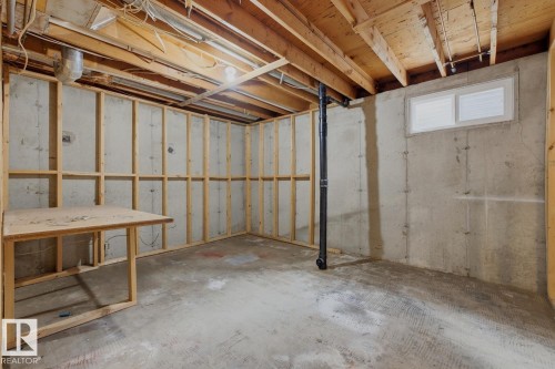 Unfinished basement featuring exposed wood ceiling joists, concrete walls, a built-in wood workbench, and a horizontal window - 10621 Beaumaris Road Nw, Edmonton, AB 