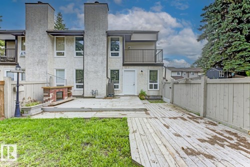 Exterior stucco finish, prominent chimney structures, upper-level balcony with metal railing, ground-level brick outdoor fireplace feature, and extensive wood decking - 10621 Beaumaris Road Nw, Edmonton, AB 
