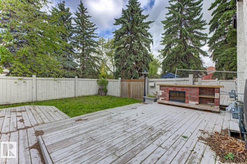 Private backyard featuring a wood deck, manicured lawn, and a built-in brick outdoor fireplace with shelving - 10621 Beaumaris Road Nw, Edmonton, AB 